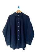 A dark navy blue long-sleeve button-up shirt hanging on a wooden hanger against a plain white wall.