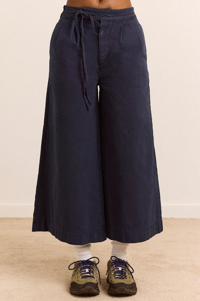 Navy blue wide-leg pants with a tie waist worn by a person on a beige background