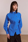 Person wearing a bright blue asymmetrical button down shirt with a plain background