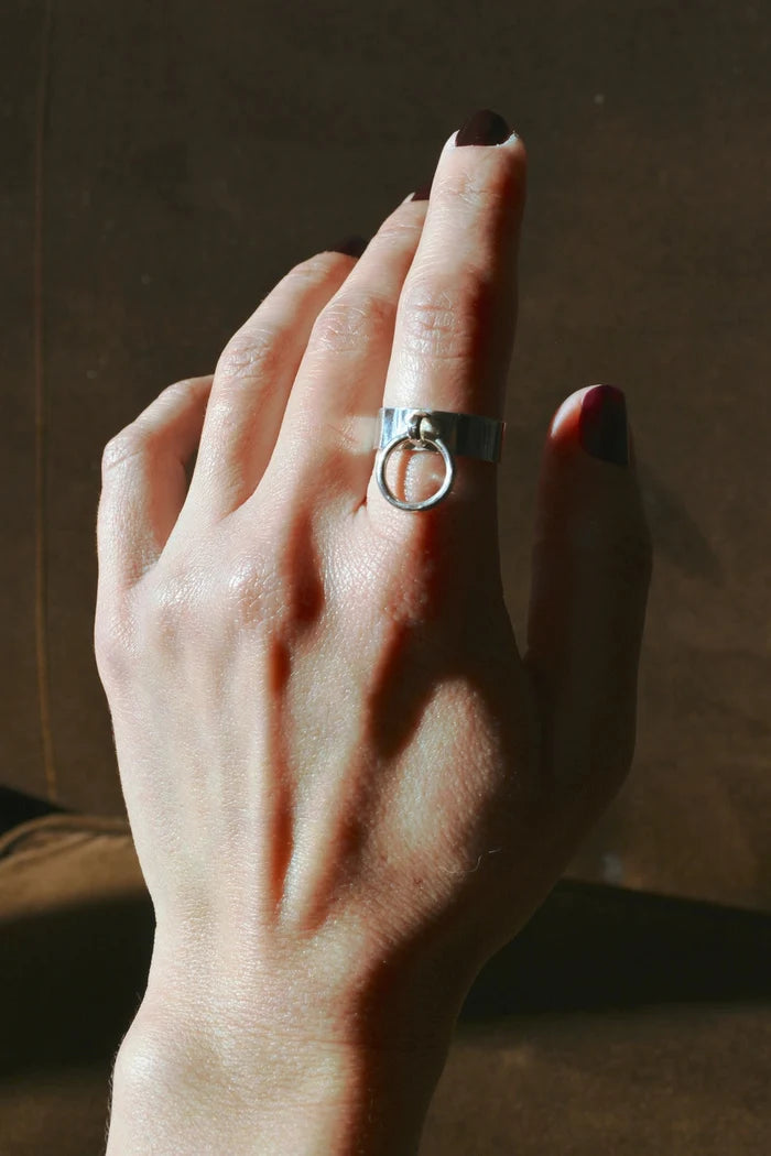 Hand wearing a silver ring with a dark background