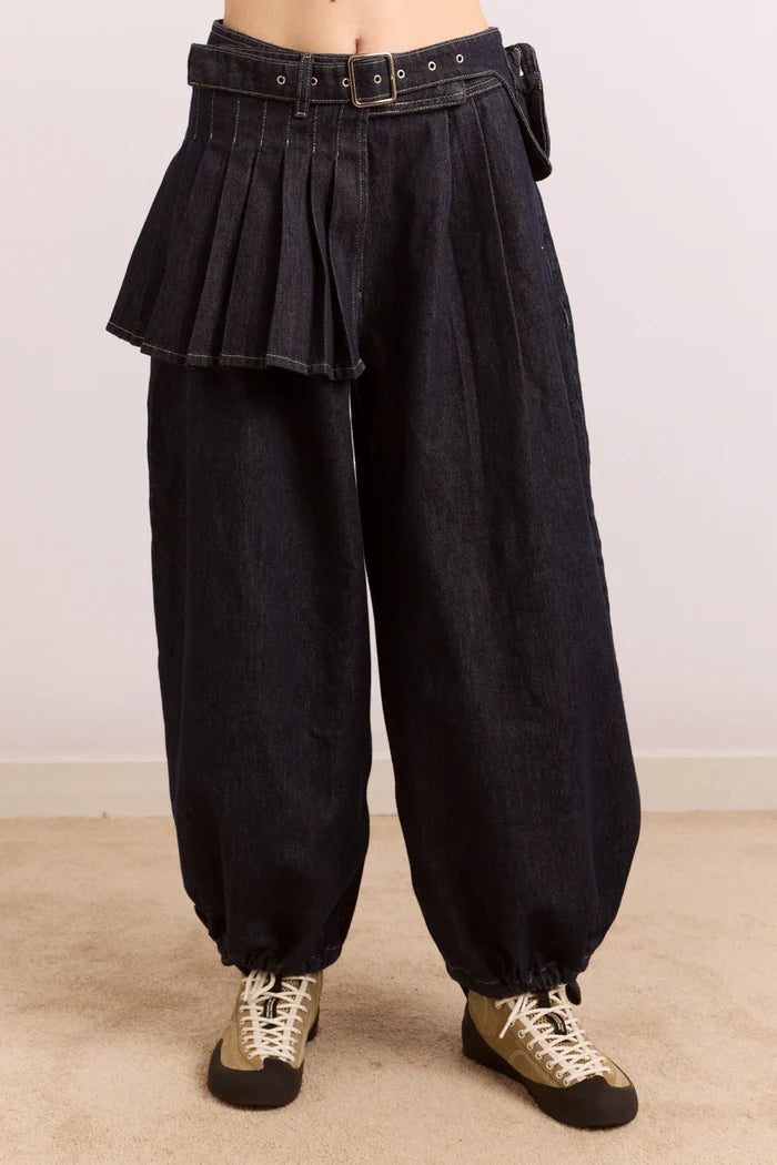 Dark blue pleated pants worn by a person on a beige floor with a neutral background