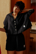 Person wearing a black outfit with a logo in a room with wooden walls and a pink garment.