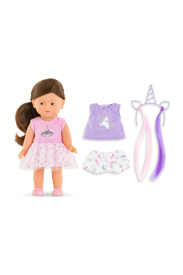 A doll outfit set displayed on a white background, featuring a doll wearing a pink unicorn-print dress, plus matching accessories including a lavender top, white shorts with rainbow prints, a horn headband, and two long hair extensions in pink and purple.