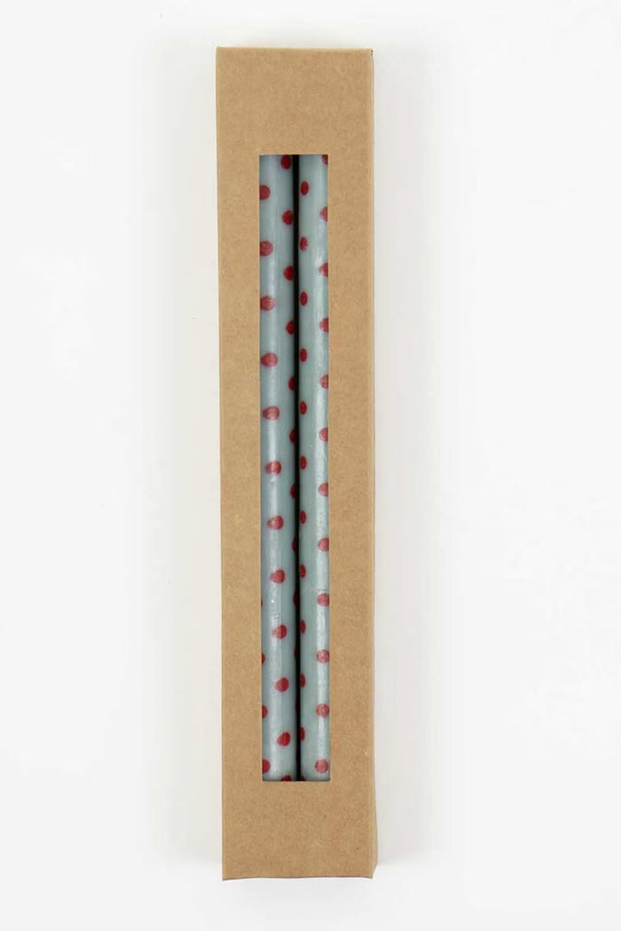 Two light blue tapered candles with red polka dots in cardboard box