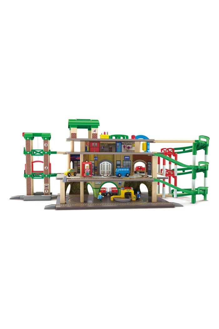 A multi-level toy train station and garage set with tracks, ramps, platforms, and small train figures, shown on a plain white background.