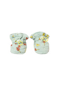 A pair of light sage green muslin baby booties with a colorful cartoon mushroom print and yellow drawstring loops, shown on a plain white background.
