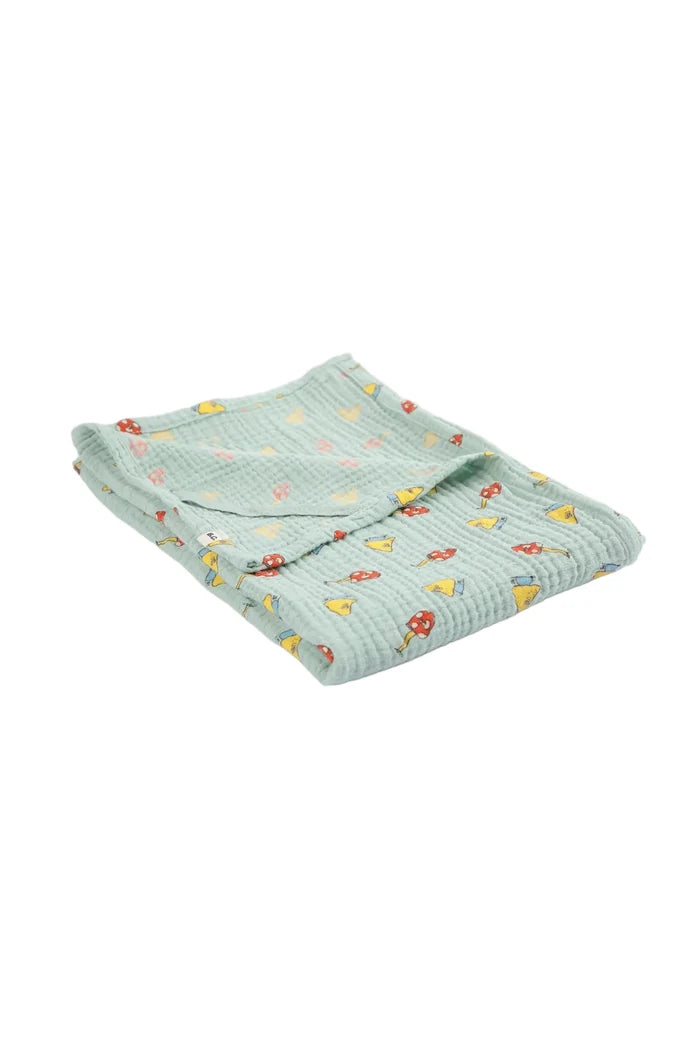 A folded light mint green waffle-weave muslin blanket with a colorful pattern of small yellow mushrooms, red mushrooms, shown on a clean white background.