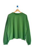 A green long-sleeve cropped sweatshirt hanging on a wooden hanger against a plain white wall.