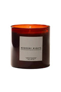 A dark amber glass candle jar with a white rectangular label reading 'NEGRONI NIGHTS' on a warm off-white background.