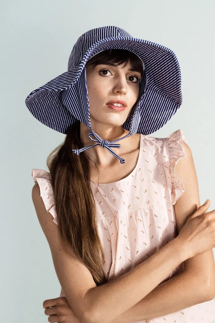 Woman wearing a blue and white striped sun hat on a light gray background