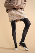 Person wearing a beige sweater, fringed skirt, black tights, and white sneakers on a beige background