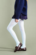 A model wearing white tights, a navy blue sweater, a dark purple pleated skirt, and dark brown leather loafers, shown from the waist down against a solid light gray-green studio background.