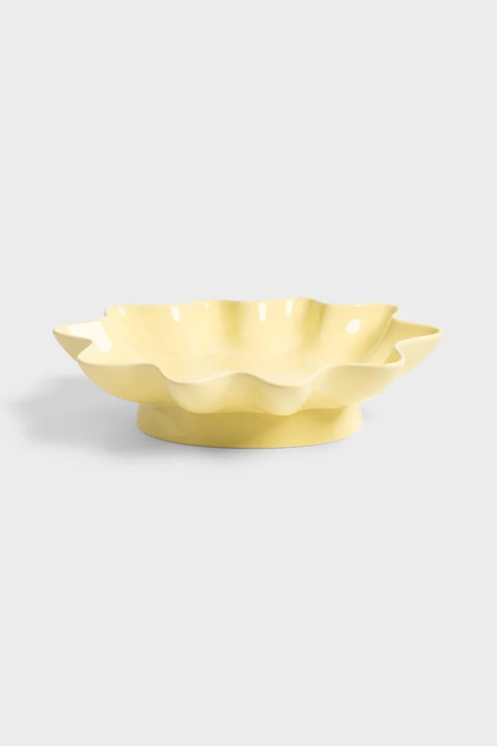 Yellow ceramic bowl with wavy edges on light grey background.