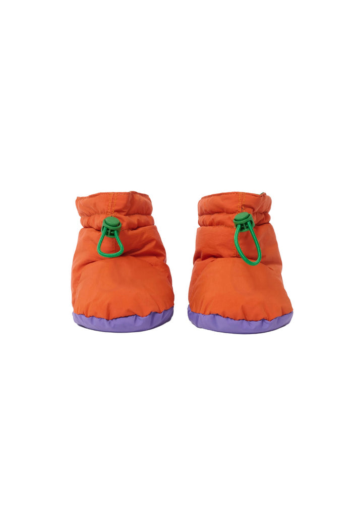 A pair of bright orange puffer boots with green drawstring loops and purple soles, shown against a plain white background.