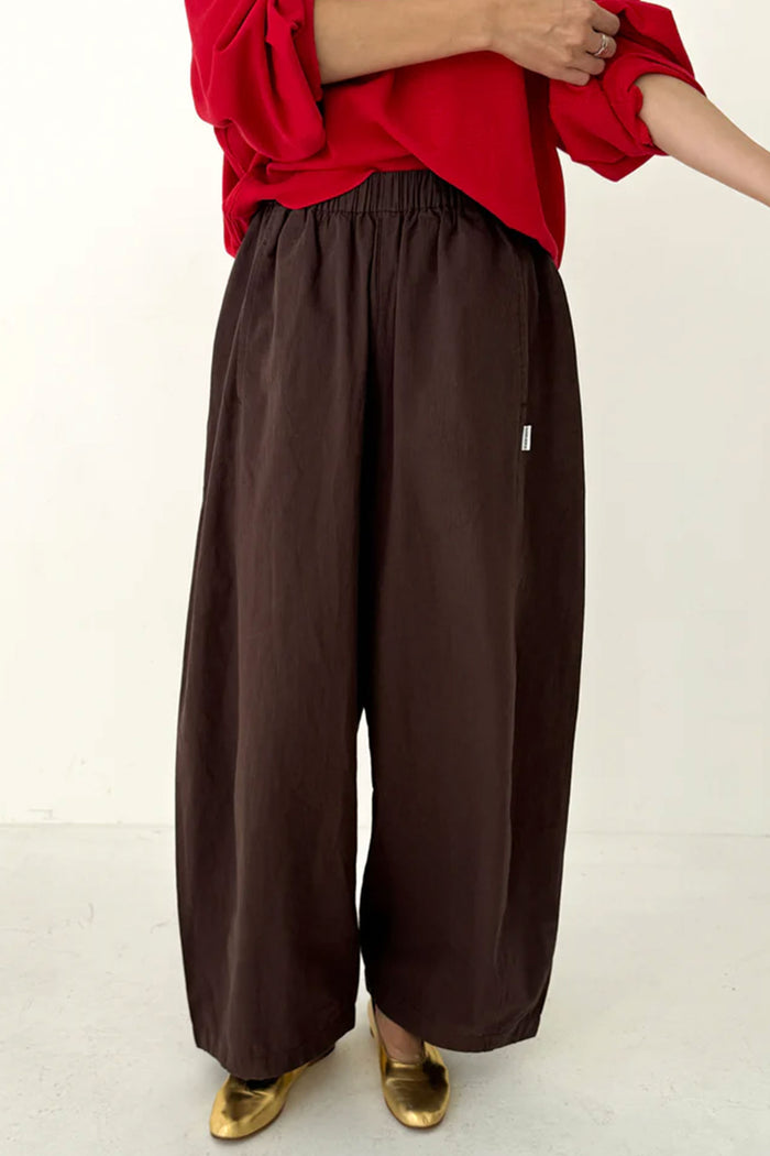 Person wearing brown wide-leg pants with a red top on a white background