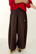 Person wearing brown wide-leg pants with a red top on a white background