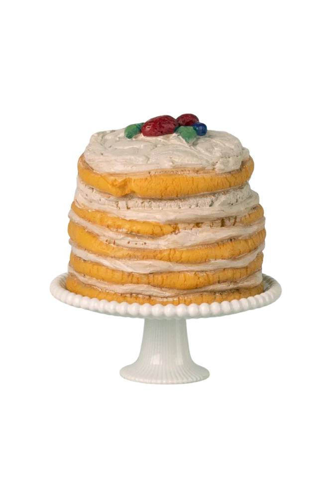 Mini layered cake with white frosting and fruit on top, placed on a white cake stand.