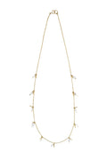 A delicate gold chain necklace featuring small, clear crystal-like leaf charms spaced along the chain, displayed against a textured off-white background.
