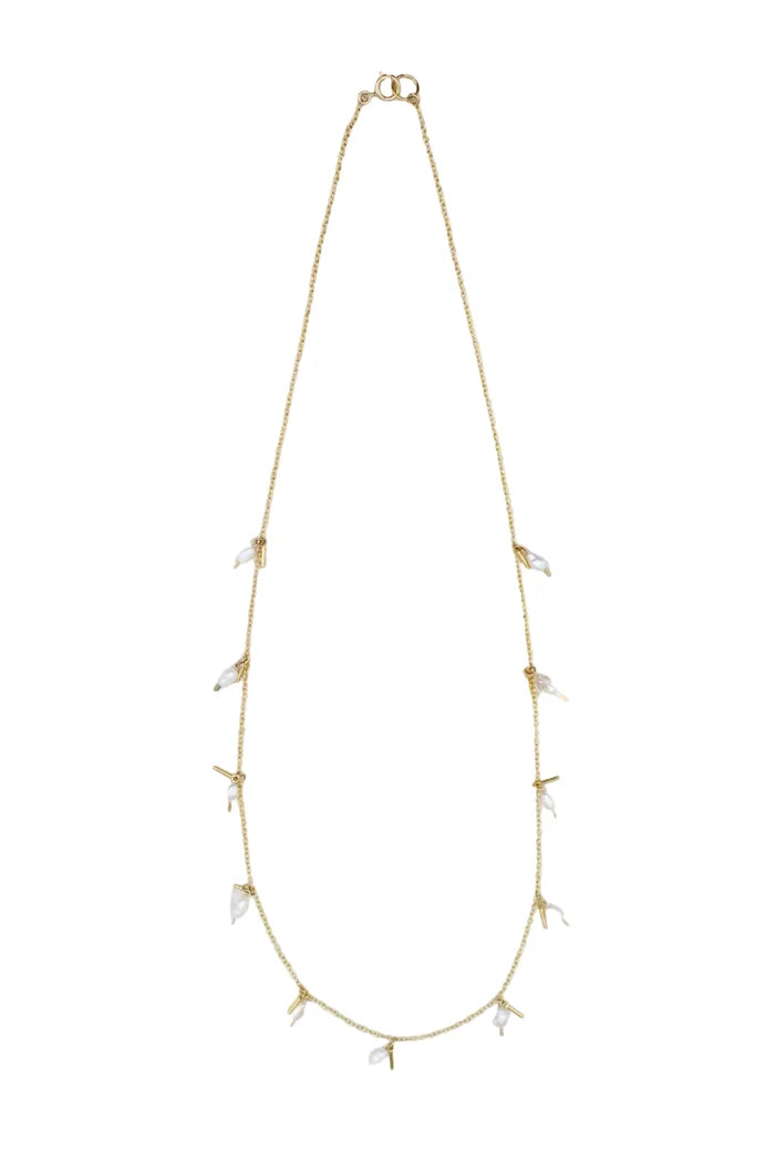A delicate gold chain necklace featuring small, clear crystal-like leaf charms spaced along the chain, displayed against a textured off-white background.