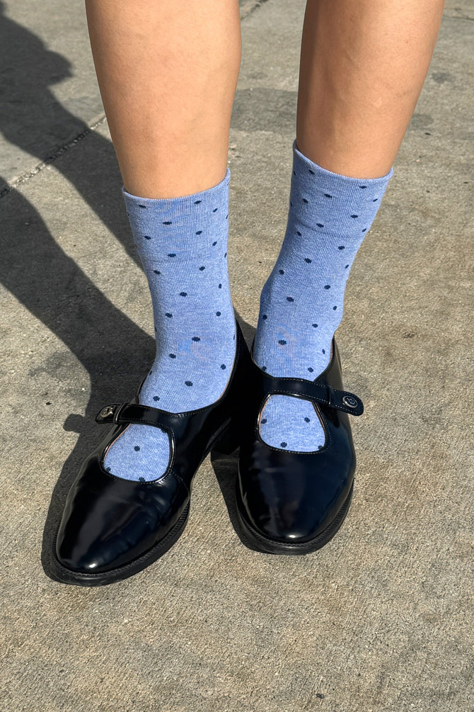 Person wearing blue polka dot socks and black shoes on a concrete surface