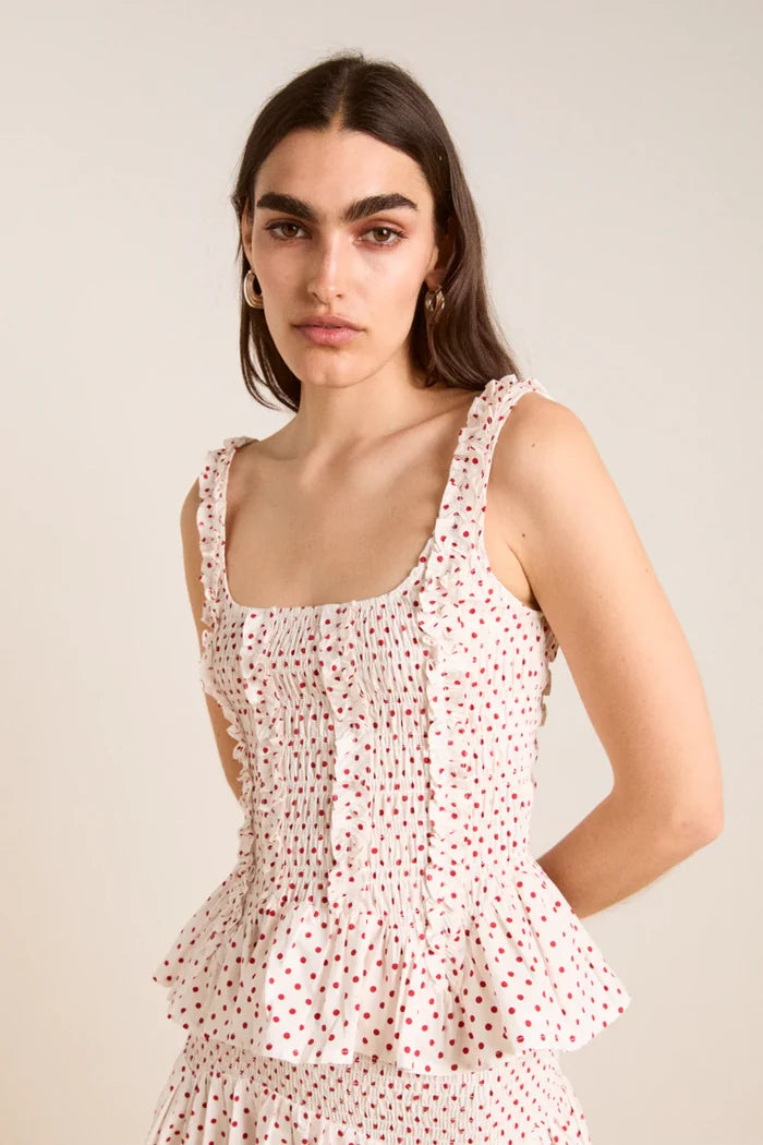 Woman wearing a white matching shirt  and skirt with red polka dots against a plain background