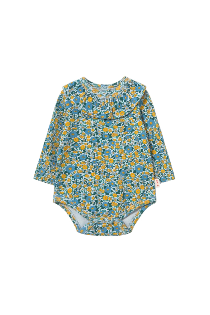 A baby long-sleeve bodysuit with a dense blue, yellow, and green floral pattern, featuring a ruffled collar, laid flat on a light cream background.