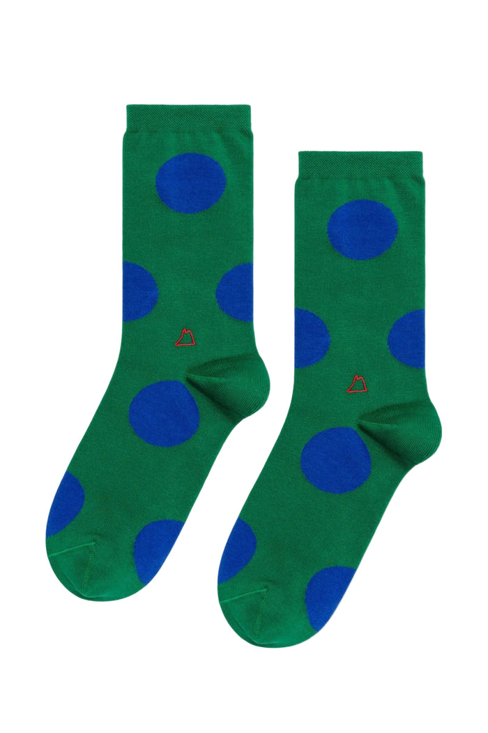 A pair of green crew socks with large blue polka dots and a small red geometric logo near the cuff, displayed against a plain white background.