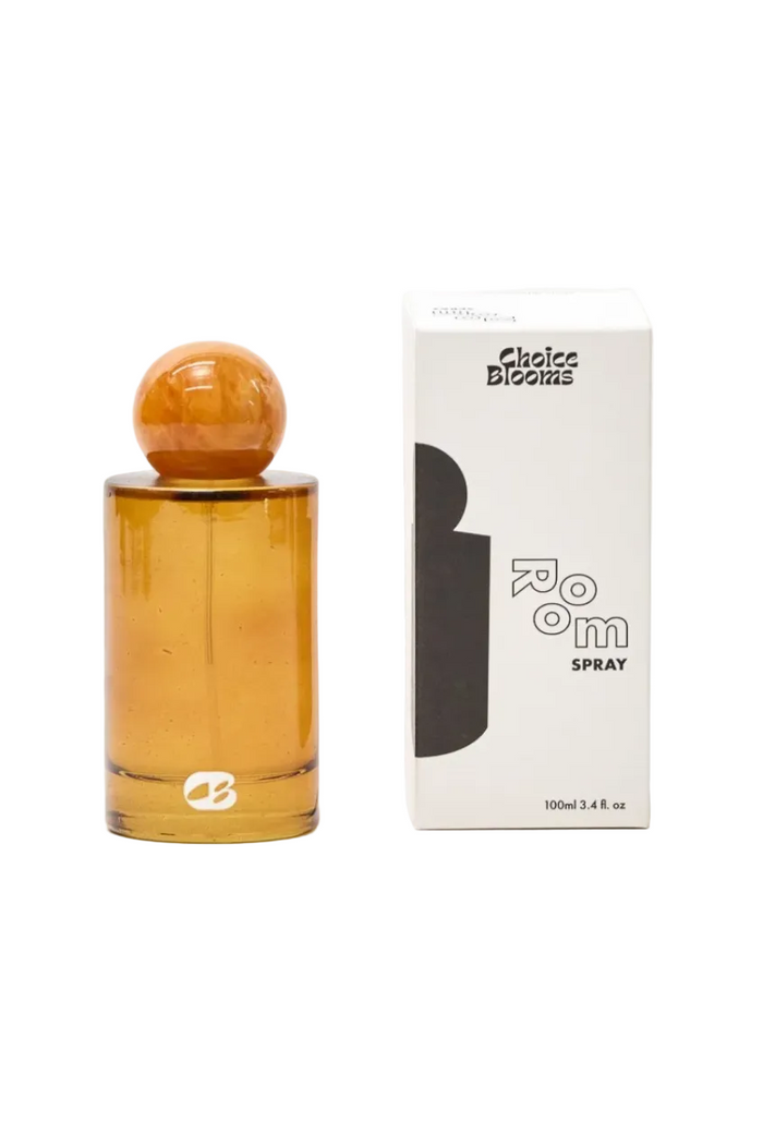 An amber glass spray bottle with a round amber cap stands next to its white packaging box against a white background