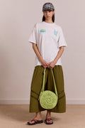 Person wearing a white t-shirt and green pants holding a green bag against a plain background