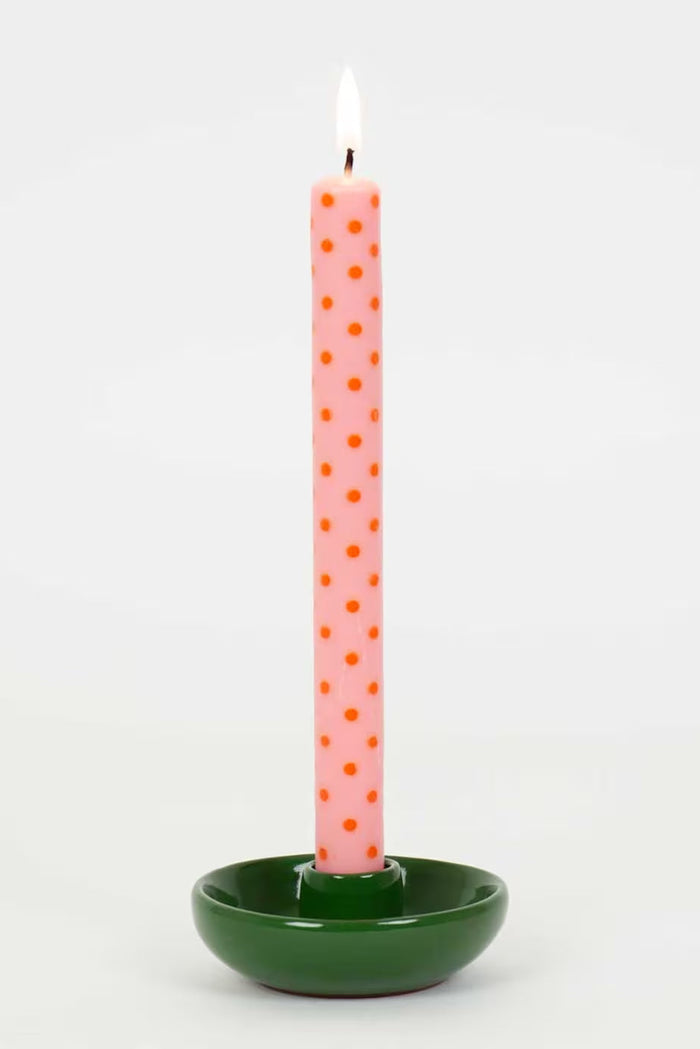 Pink polka dot candle in a green holder on a white background