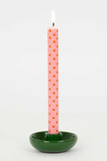 Pink polka dot candle in a green holder on a white background