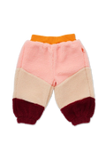 A pair of children's sherpa pants in a color-blocked design with a pink upper section, a beige middle section, a dark red lower section, and an orange elastic waistband, shown against a plain white background.