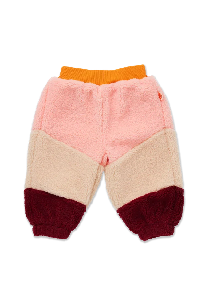 A pair of children's sherpa pants in a color-blocked design with a pink upper section, a beige middle section, a dark red lower section, and an orange elastic waistband, shown against a plain white background.