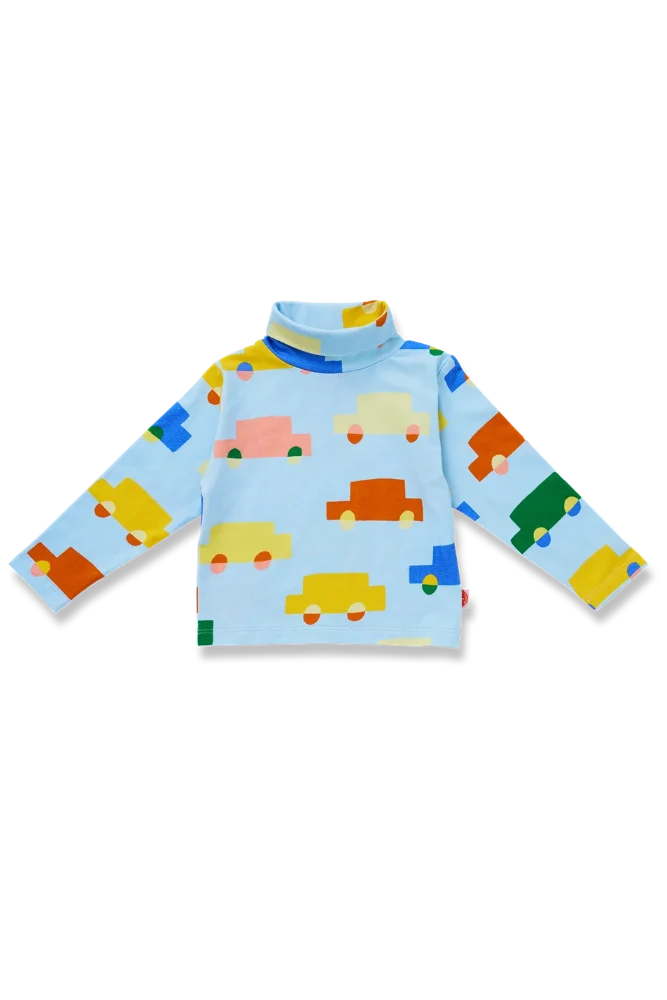 A light blue long-sleeve turtleneck top for toddlers, featuring a playful pattern of colorful cartoon cars in yellow, orange, green, pink, and blue.