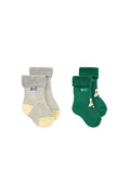 Two pairs of children's socks on a light gray background. The left pair is gray and white striped with a yellow toe and heel, featuring a fuzzy gray cuff and 'BC' in blue.