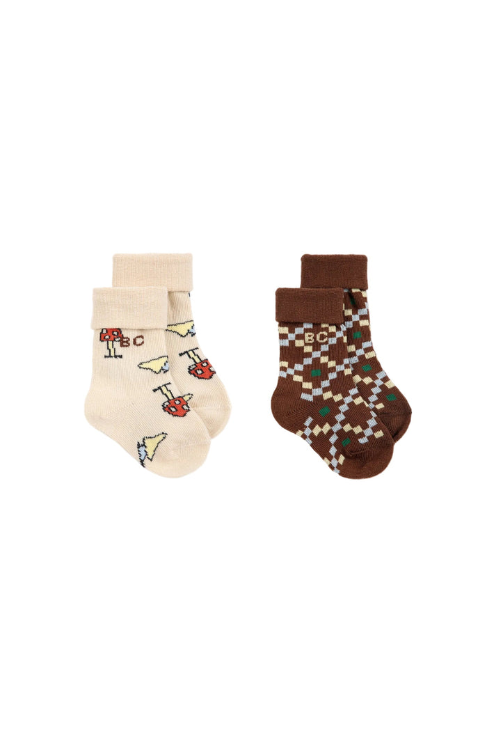 A 2-pack of children's socks on a white background, featuring one cream-colored sock with colorful cartoon motifs and one brown argyle patterned sock with a matching cuff.