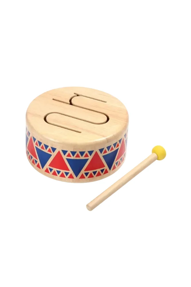 A small wooden toy drum with a natural wood finish, decorated with red and blue geometric triangle patterns on the side, shown with a matching wooden mallet that has a yellow ball tip on a white background.