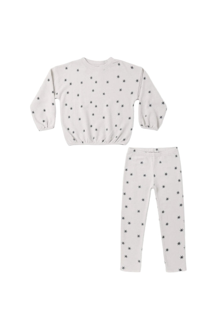 A two-piece children's set featuring a long-sleeve top and matching pants in a light off-white fabric with a small black star pattern, laid flat on a white background.