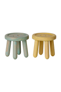 Two small round wooden stools with short legs, shown side by side on a white background. The stool on the left has a distressed light blue-green finish, and the stool on the right has a natural light wood finish.