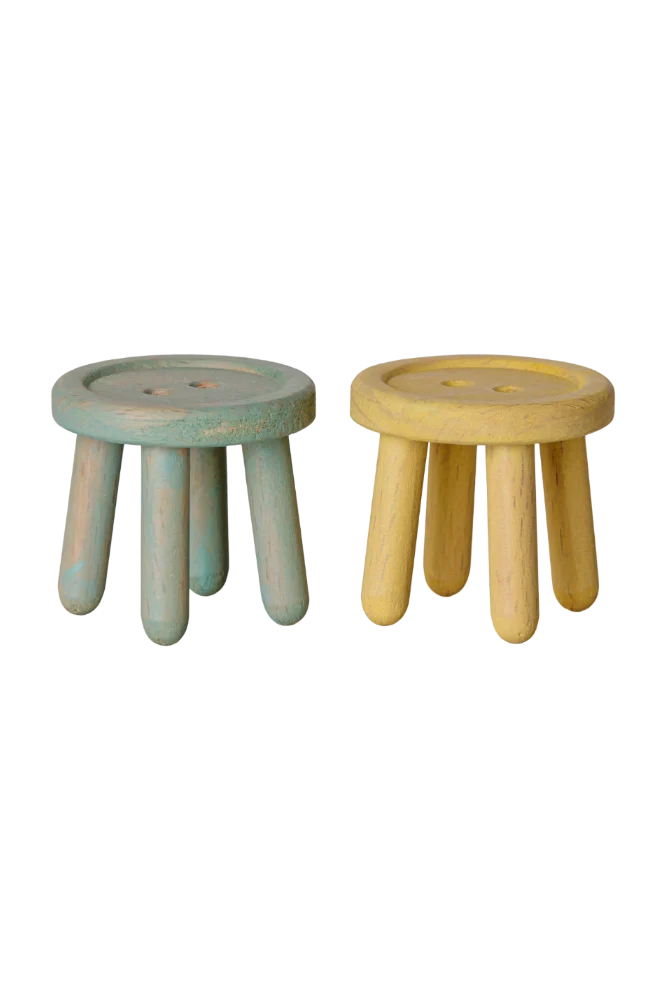 Two small round wooden stools with short legs, shown side by side on a white background. The stool on the left has a distressed light blue-green finish, and the stool on the right has a natural light wood finish.