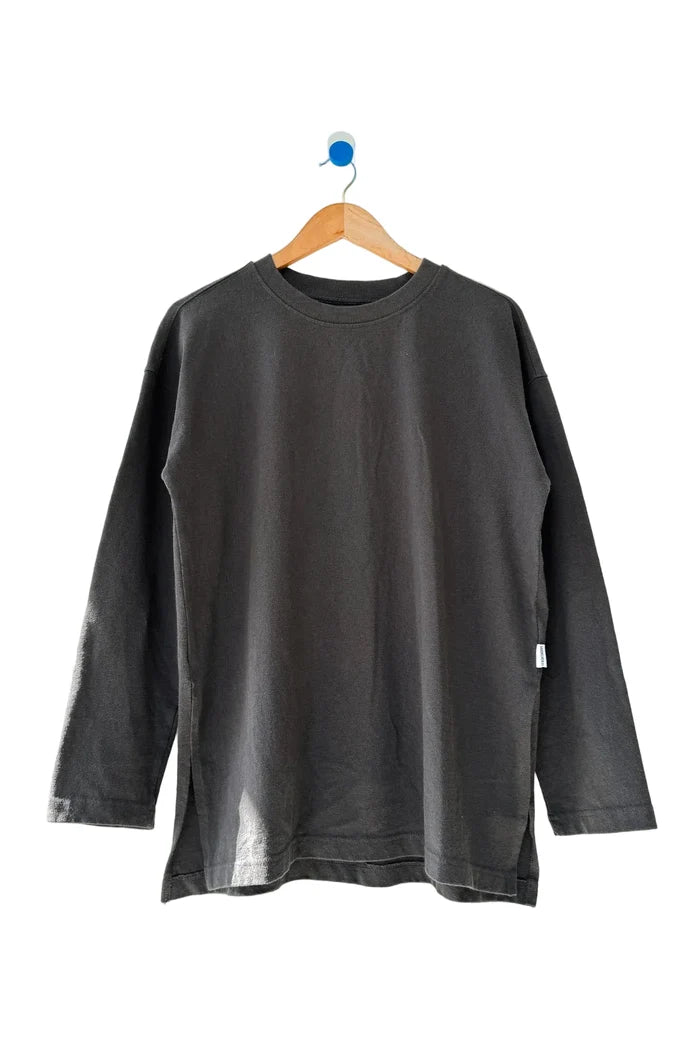 A dark charcoal gray long-sleeve crewneck shirt hanging on a wooden hanger against a plain off-white wall.