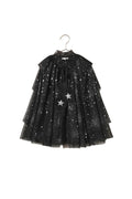 A black tulle dress with silver glitter stars and two silver star appliqués, hanging on a metal hanger against a textured beige wall.