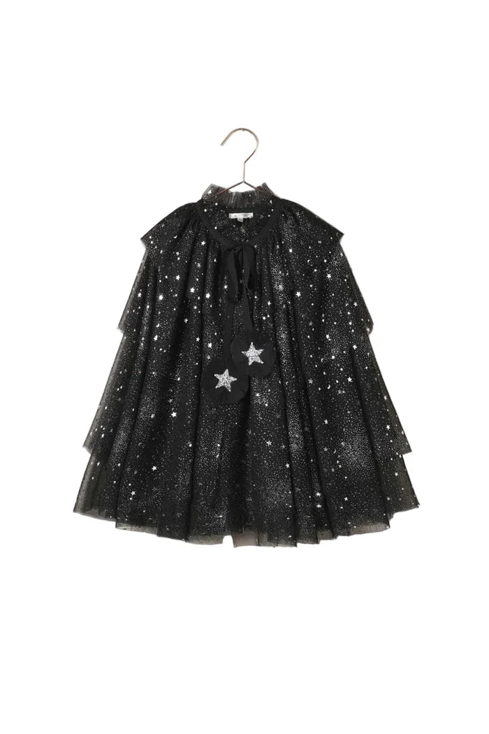 A black tulle dress with silver glitter stars and two silver star appliqués, hanging on a metal hanger against a textured beige wall.