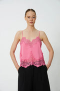 Woman wearing bright pink lace camisole and black pants against white background