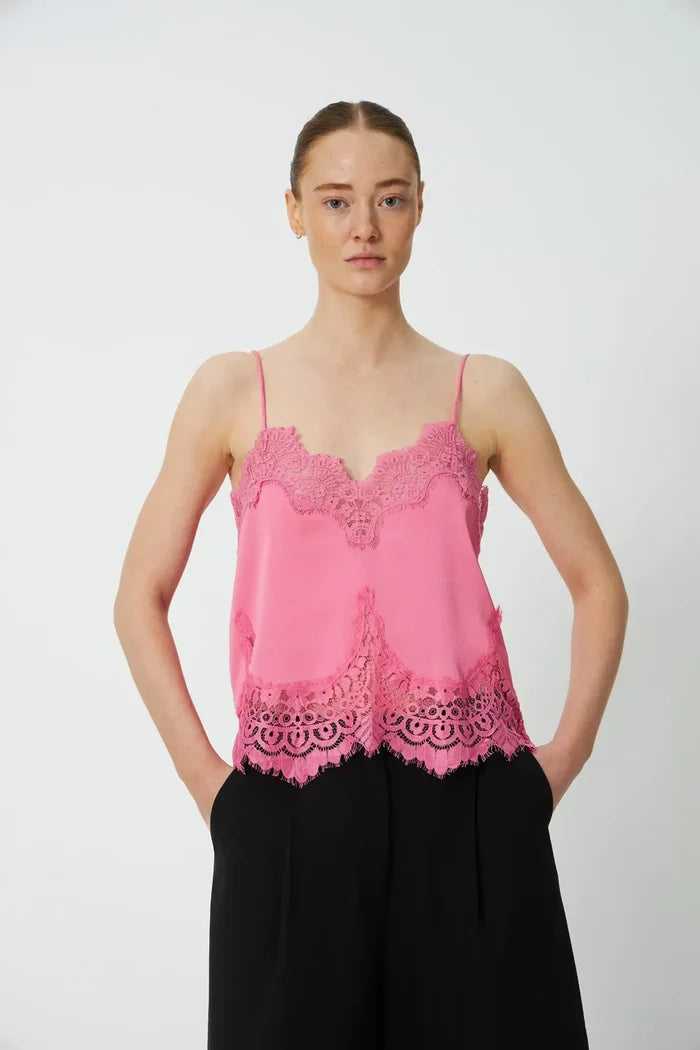 Woman wearing bright pink lace camisole and black pants against white background