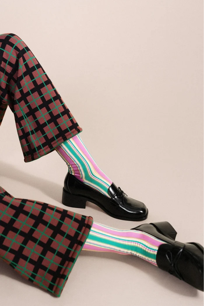Person wearing plaid pants, striped socks, and black shoes on a beige background