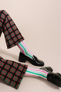 Person wearing plaid pants, striped socks, and black shoes on a beige background