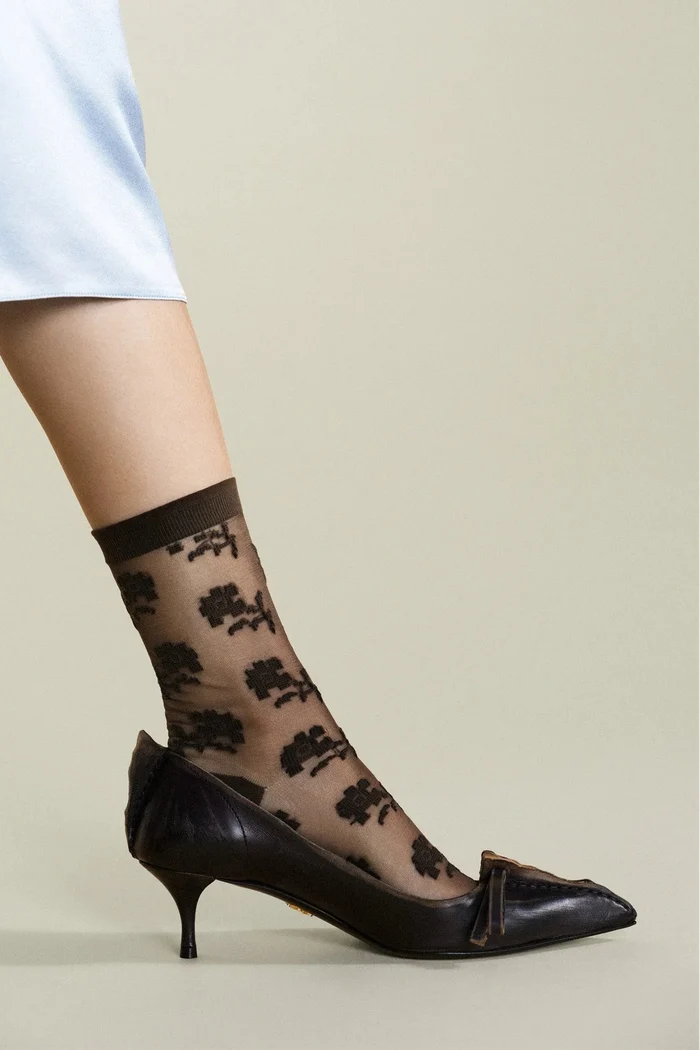 Black floral-patterned sheer socks worn with black high-heeled shoes on a neutral background