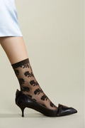 Black floral-patterned sheer socks worn with black high-heeled shoes on a neutral background