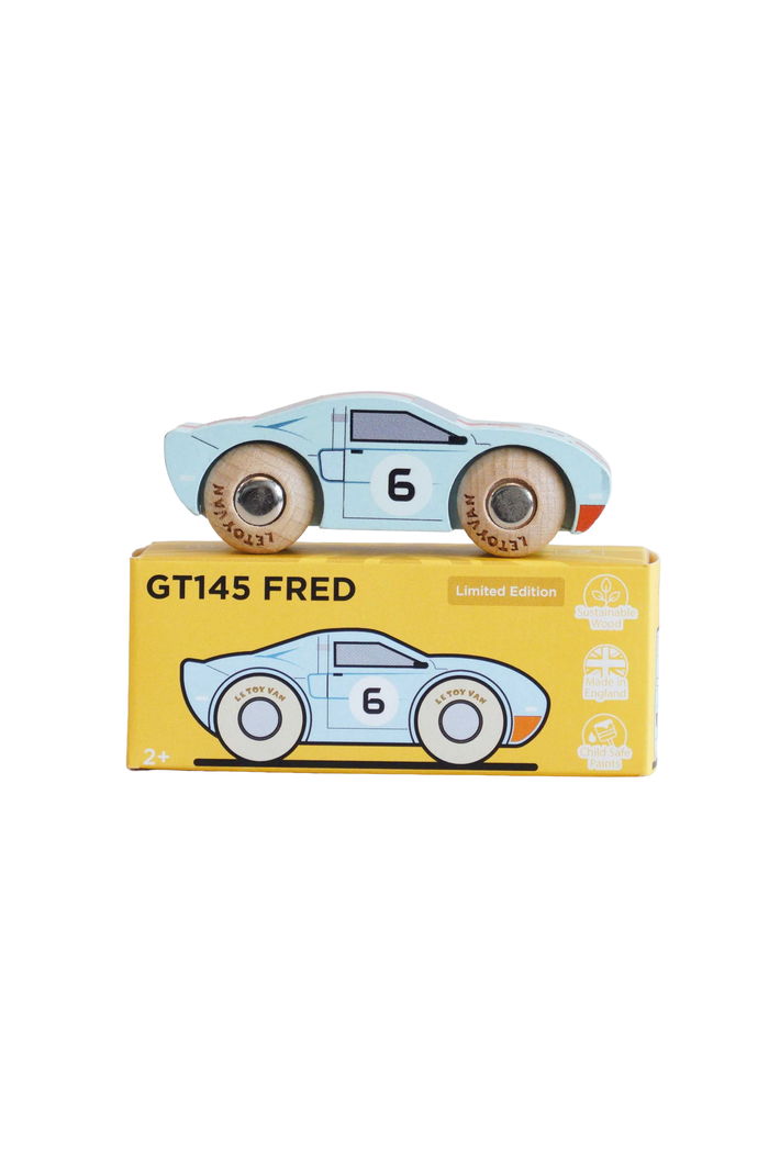 A wooden toy race car named GT145 Fred, painted in light blue with the number 6, displayed on top of its yellow packaging box against a white background.